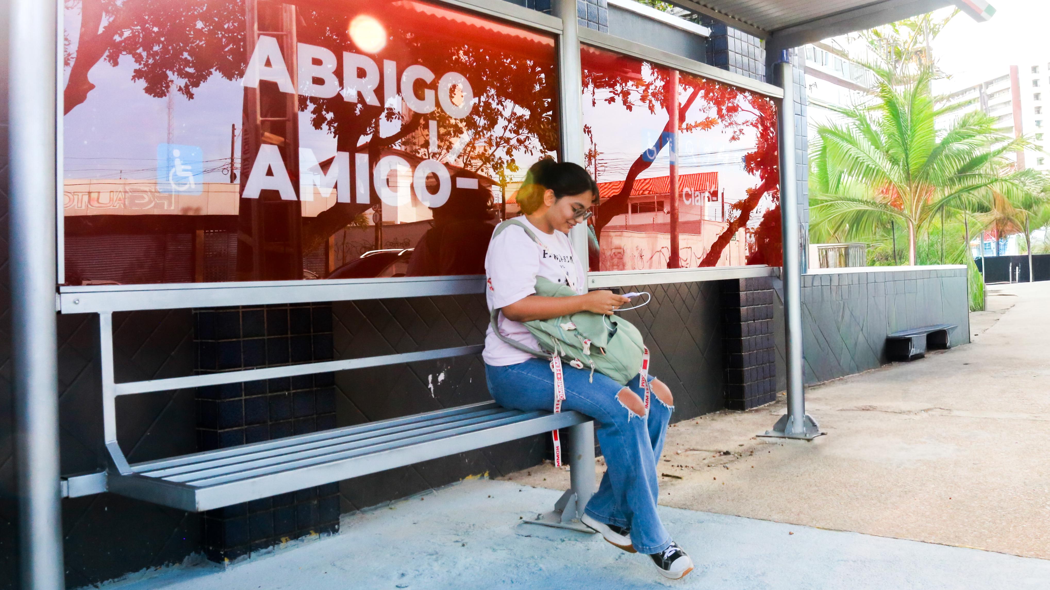 Mulher sentada em uma parada de ônibus do Abrigo Amigo